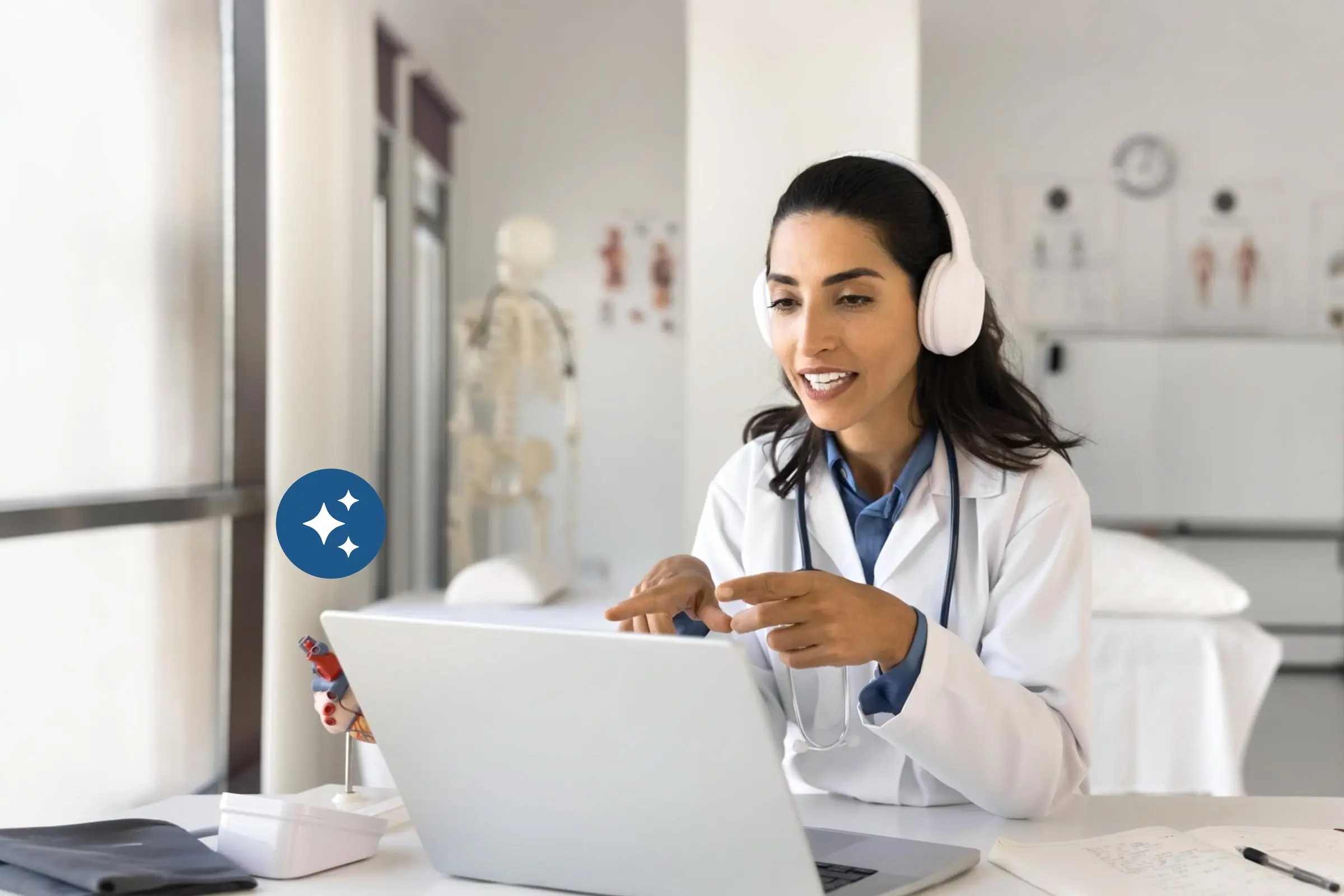 Female physician with headphones running a telehealth visit on her laptop in the exam room &mdash; eCareAssist hybrid care platform handles both virtual and in-person appointments